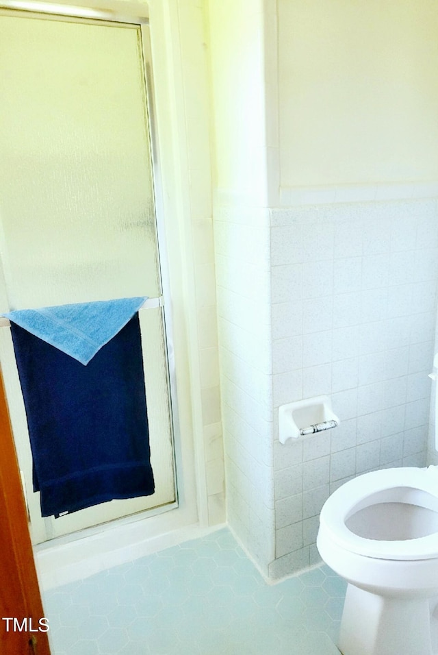 bathroom featuring a wainscoted wall, tile walls, toilet, a shower stall, and tile patterned flooring