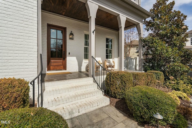 view of exterior entry featuring brick siding and a porch