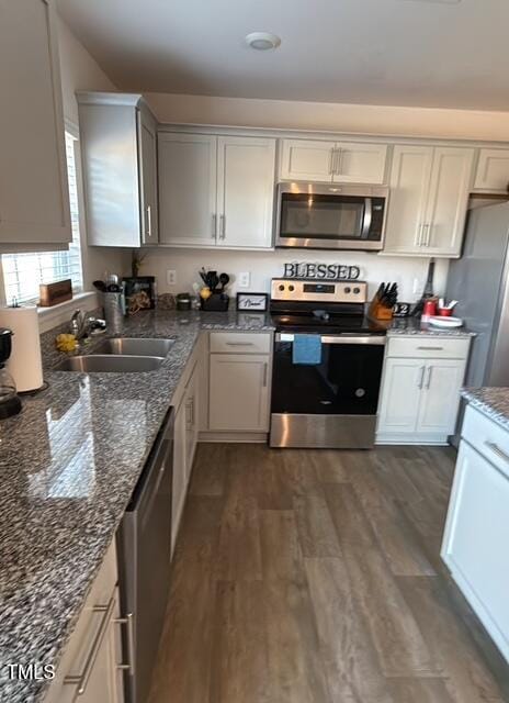 kitchen with appliances with stainless steel finishes, dark wood-type flooring, a sink, and dark stone countertops