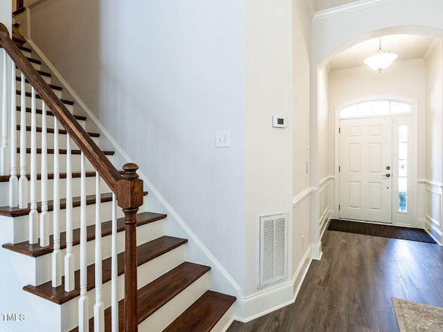 foyer entrance with visible vents, arched walkways, dark wood-type flooring, and ornamental molding