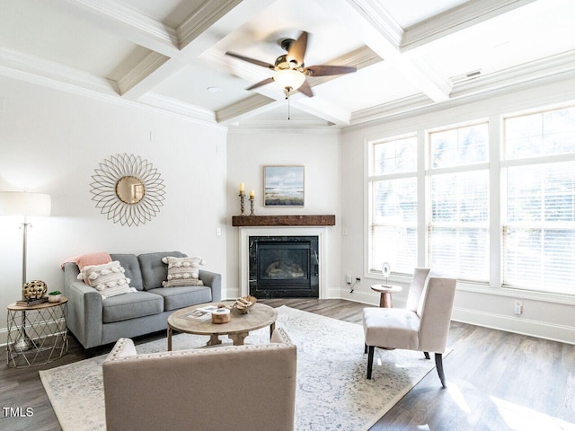 living room featuring a glass covered fireplace, beamed ceiling, baseboards, and wood finished floors