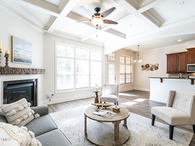 living area with beam ceiling, a fireplace, light wood finished floors, coffered ceiling, and baseboards