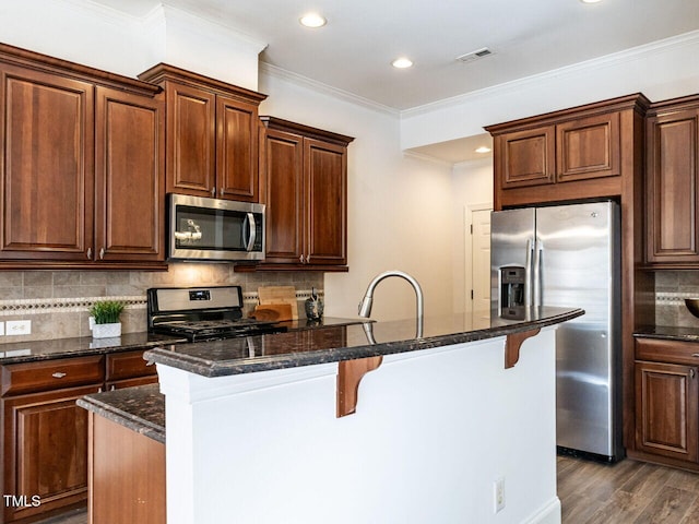 kitchen featuring dark wood finished floors, stainless steel appliances, decorative backsplash, ornamental molding, and a kitchen breakfast bar