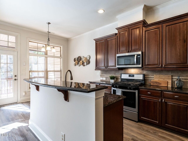 kitchen with dark wood-style flooring, stainless steel appliances, decorative backsplash, ornamental molding, and a kitchen breakfast bar