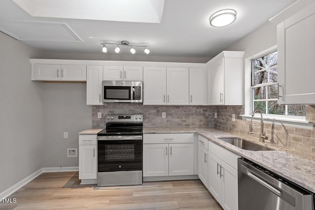 kitchen featuring tasteful backsplash, appliances with stainless steel finishes, light wood-type flooring, white cabinetry, and a sink