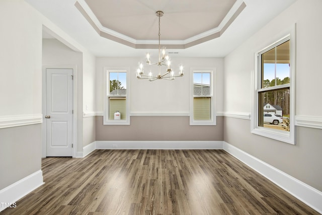 unfurnished dining area featuring baseboards, a tray ceiling, a wealth of natural light, and wood finished floors