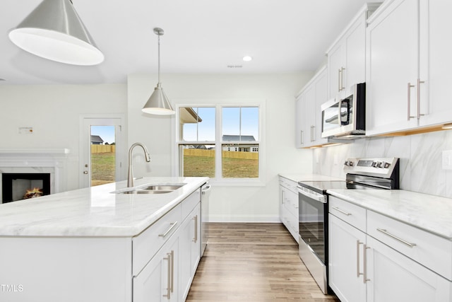 kitchen with a premium fireplace, wood finished floors, a sink, white cabinetry, and appliances with stainless steel finishes