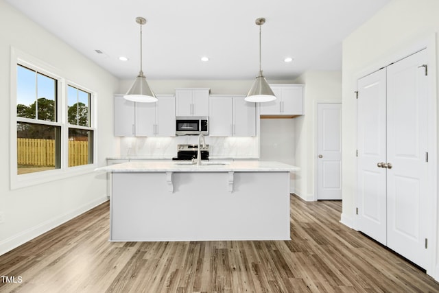 kitchen with stainless steel appliances, wood finished floors, a sink, white cabinetry, and decorative backsplash