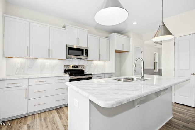 kitchen with light wood-type flooring, a kitchen island with sink, appliances with stainless steel finishes, and a sink