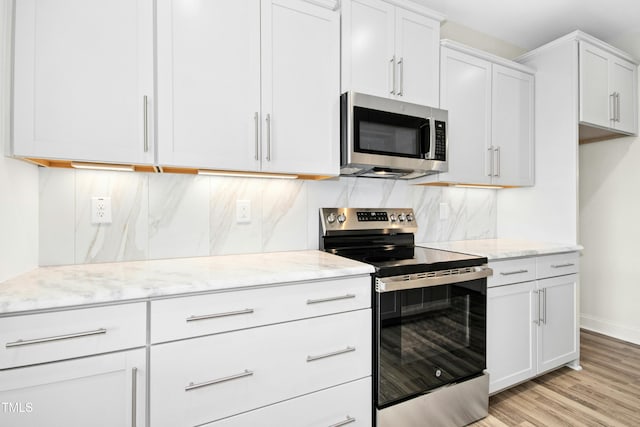 kitchen with light wood-style floors, tasteful backsplash, appliances with stainless steel finishes, and light stone counters