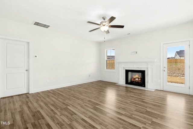 unfurnished living room with a fireplace, wood finished floors, visible vents, baseboards, and a ceiling fan