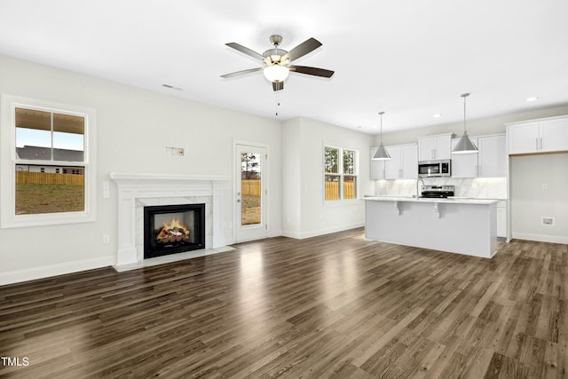 unfurnished living room with dark wood-style floors, visible vents, ceiling fan, and baseboards