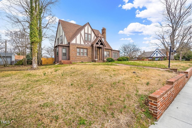 tudor home with a shingled roof, a chimney, crawl space, fence, and brick siding