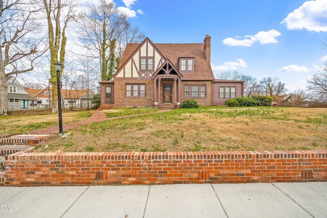 tudor home featuring brick siding, roof with shingles, a chimney, stucco siding, and a front yard