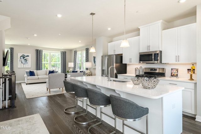 kitchen with stainless steel appliances, dark wood-style flooring, a sink, light countertops, and an island with sink