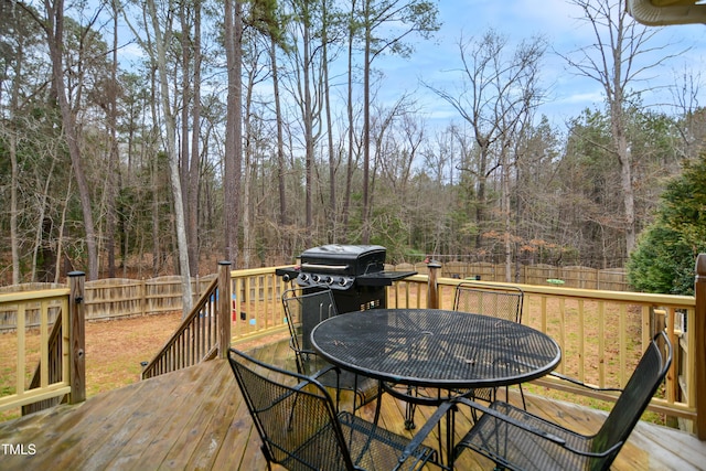 deck featuring outdoor dining space, a fenced backyard, a wooded view, and area for grilling