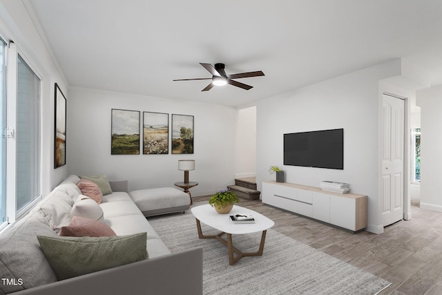 living area featuring ceiling fan, stairway, baseboards, and light wood-style flooring