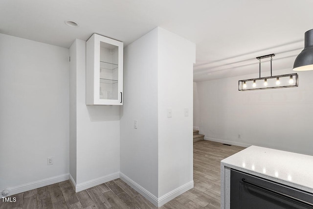 interior space with glass insert cabinets, baseboards, light wood finished floors, and pendant lighting