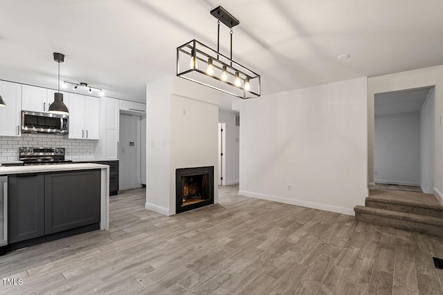 kitchen featuring light wood-style flooring, a fireplace, appliances with stainless steel finishes, open floor plan, and backsplash