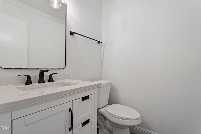 half bathroom featuring baseboards, toilet, vanity, and crown molding