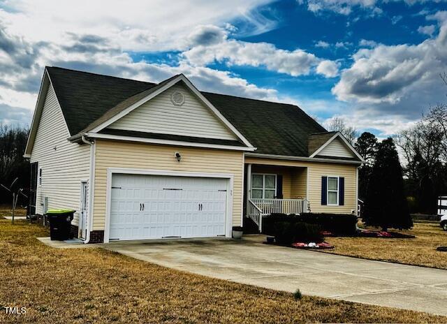 view of front of house with an attached garage, covered porch, a front lawn, and concrete driveway