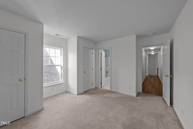 unfurnished bedroom featuring a textured ceiling, baseboards, visible vents, and light colored carpet