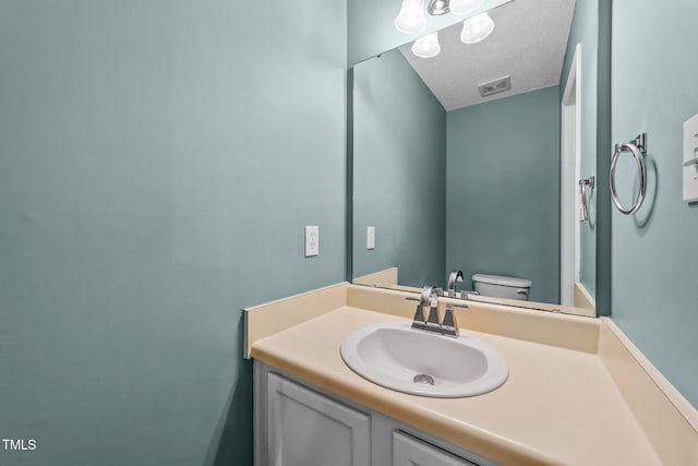 bathroom with a textured ceiling, visible vents, vanity, and toilet