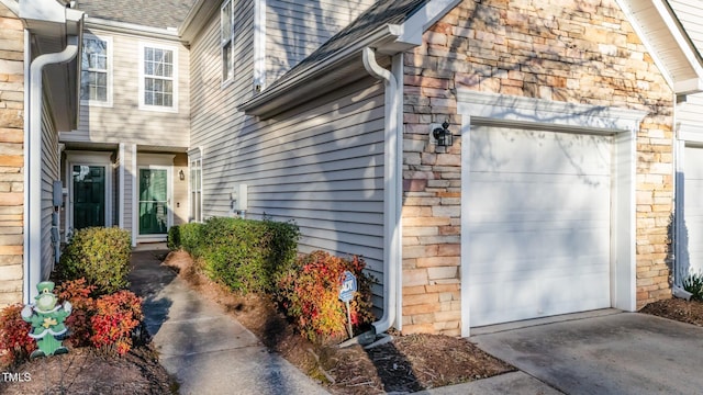 property entrance featuring a garage, stone siding, and roof with shingles