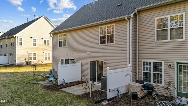 back of property with central air condition unit, roof with shingles, a lawn, and a patio