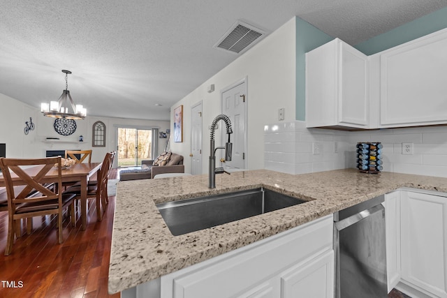 kitchen with dark wood finished floors, visible vents, stainless steel dishwasher, open floor plan, and a sink