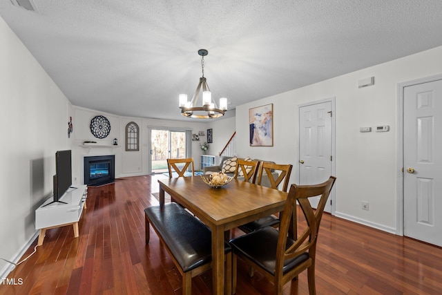 dining room with an inviting chandelier, a textured ceiling, dark wood-style flooring, and a glass covered fireplace