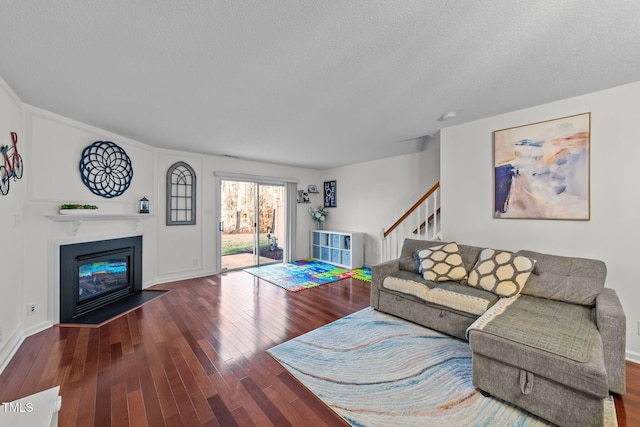 living room featuring a textured ceiling, hardwood / wood-style floors, a fireplace with flush hearth, and stairs