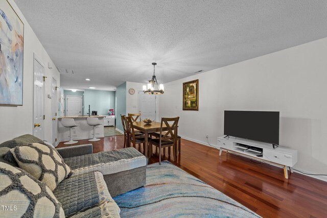 living area with visible vents, an inviting chandelier, a textured ceiling, wood finished floors, and baseboards