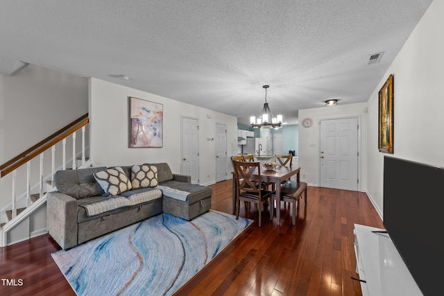 living room featuring dark wood-style floors, stairs, visible vents, and a notable chandelier