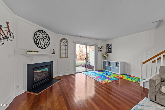 living room featuring baseboards, visible vents, a glass covered fireplace, stairway, and hardwood / wood-style floors