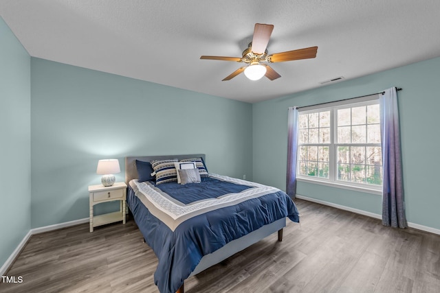 bedroom featuring ceiling fan, wood finished floors, visible vents, and baseboards