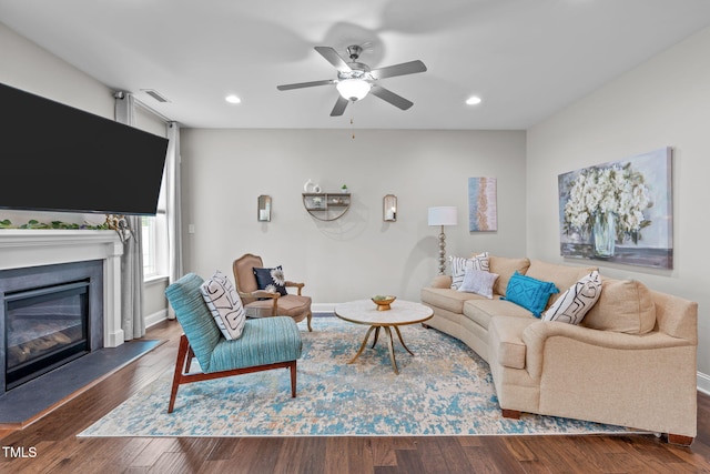 living area featuring a glass covered fireplace, ceiling fan, wood finished floors, baseboards, and recessed lighting