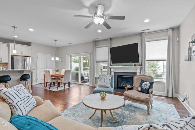 living room with a ceiling fan, recessed lighting, dark wood-style flooring, baseboards, and a fireplace with flush hearth