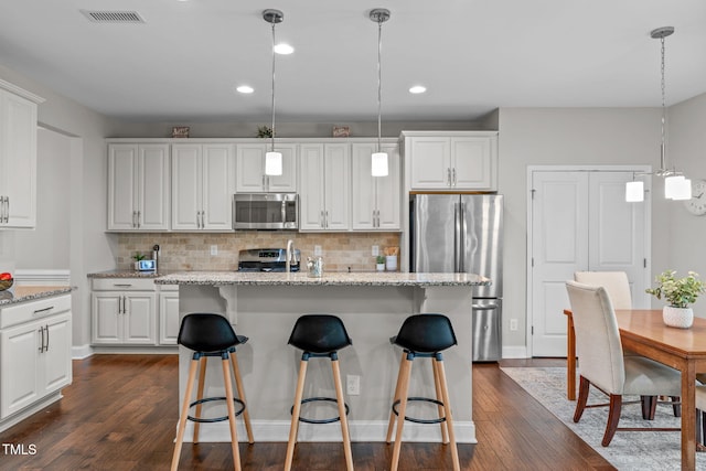 kitchen featuring appliances with stainless steel finishes, dark wood-style floors, tasteful backsplash, a kitchen bar, and white cabinets