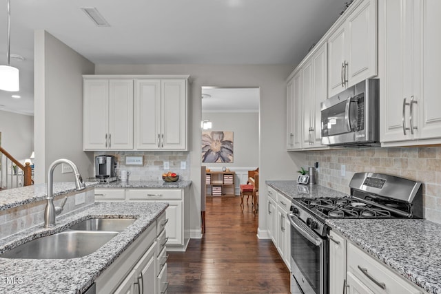 kitchen with appliances with stainless steel finishes, a sink, white cabinetry, dark wood-type flooring, and backsplash