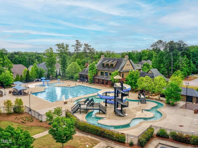 community pool with fence, a water play area, a water slide, and view of wooded area