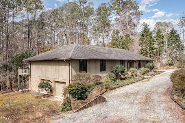 view of property exterior featuring a garage, brick siding, driveway, and a shingled roof