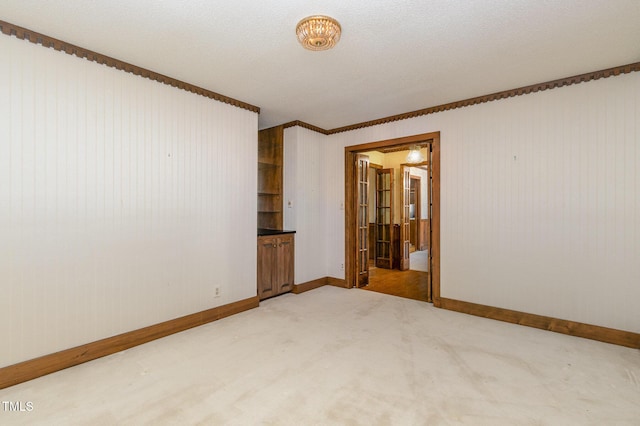 empty room with light carpet, a textured ceiling, and baseboards