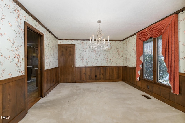 unfurnished room featuring wallpapered walls, visible vents, wainscoting, an inviting chandelier, and carpet flooring