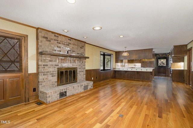 unfurnished living room featuring a brick fireplace, wainscoting, and wood finished floors