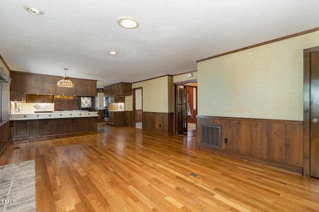 unfurnished living room featuring a textured ceiling, visible vents, wood finished floors, and wainscoting