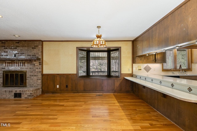 kitchen with light wood-style flooring, a wainscoted wall, visible vents, light countertops, and a brick fireplace