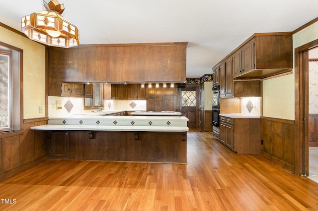 kitchen featuring wainscoting, wood finished floors, a peninsula, light countertops, and a sink