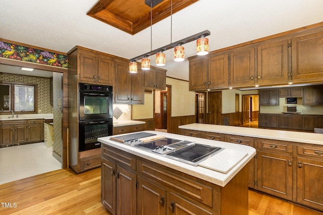 kitchen with dobule oven black, a sink, wainscoting, a center island, and stovetop with downdraft