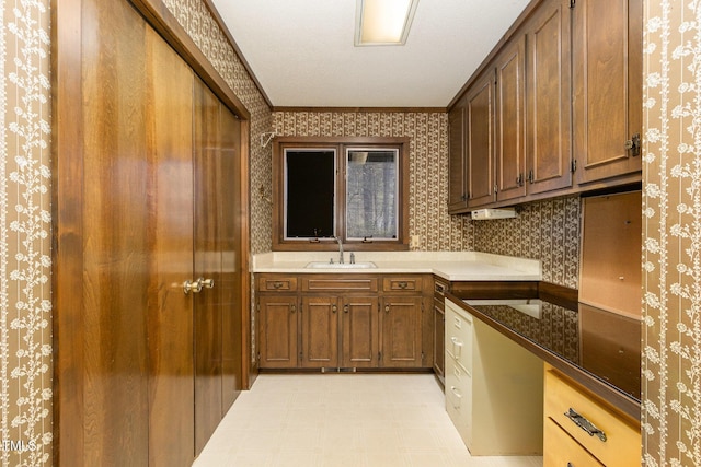 kitchen with a sink, ornamental molding, brown cabinets, light floors, and wallpapered walls